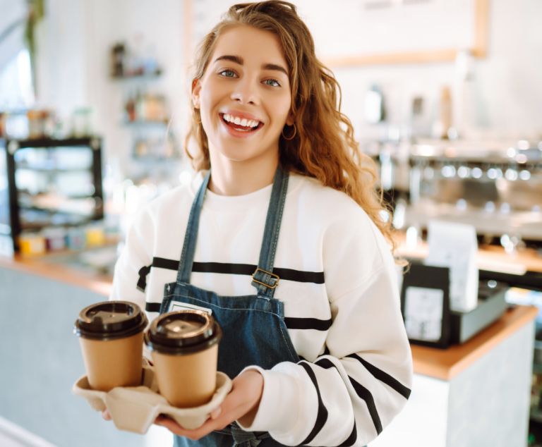 The happy barista holding two cups of coffee in a growing café